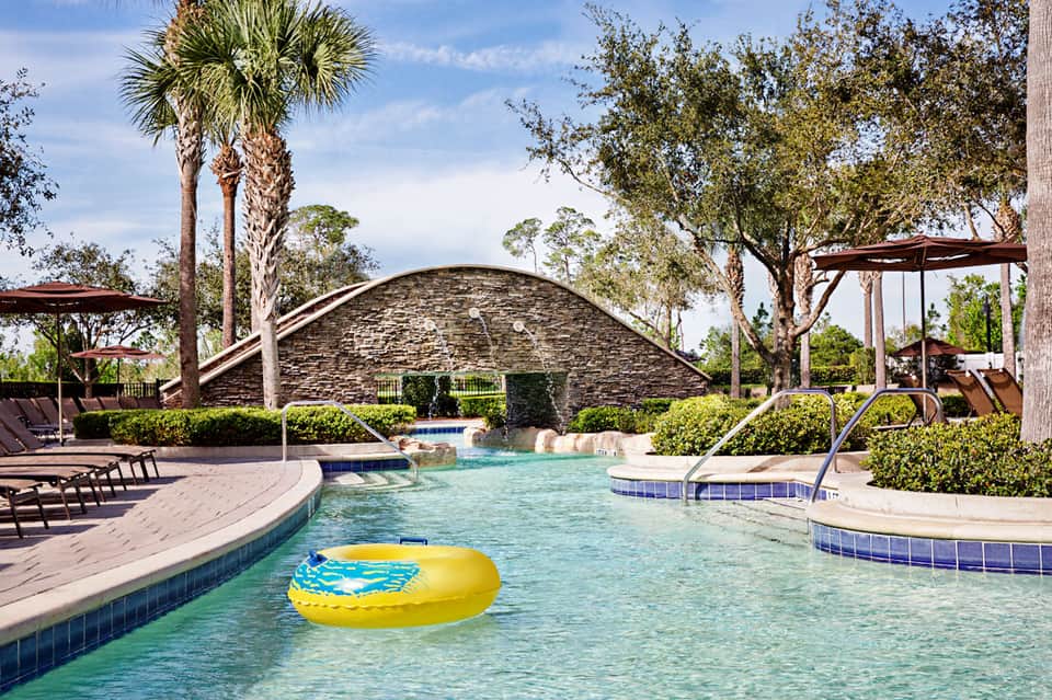 Luxurious resort pool with curved architecture, palm trees, lounge chairs, and tropical landscaping under blue sky