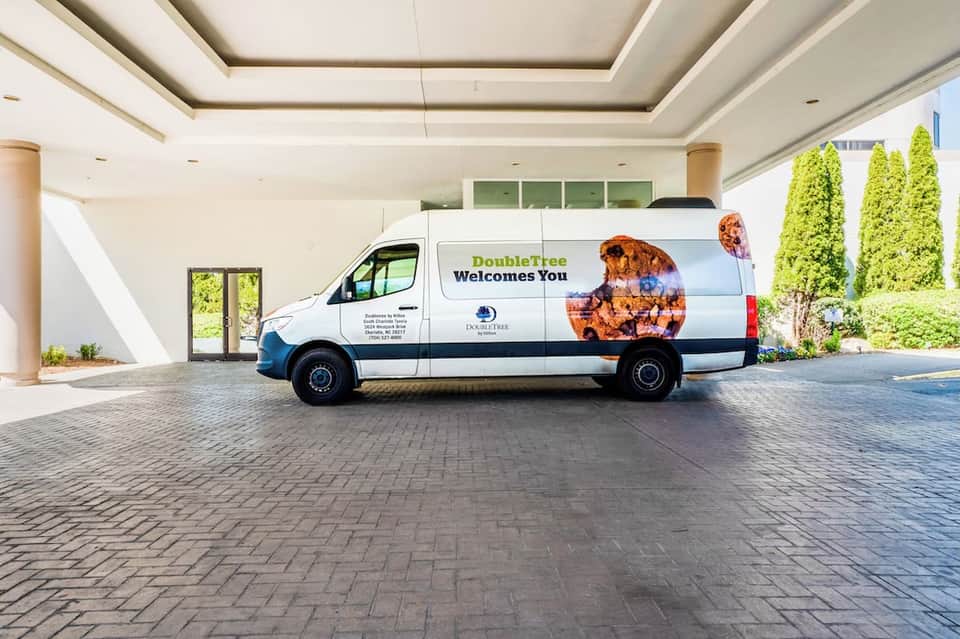 Hotel entrance with porte-cochere ceiling and white shuttle van with welcome message