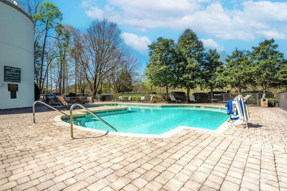 Community pool with turquoise water, metal railings, lounge chairs, and wooded surroundings