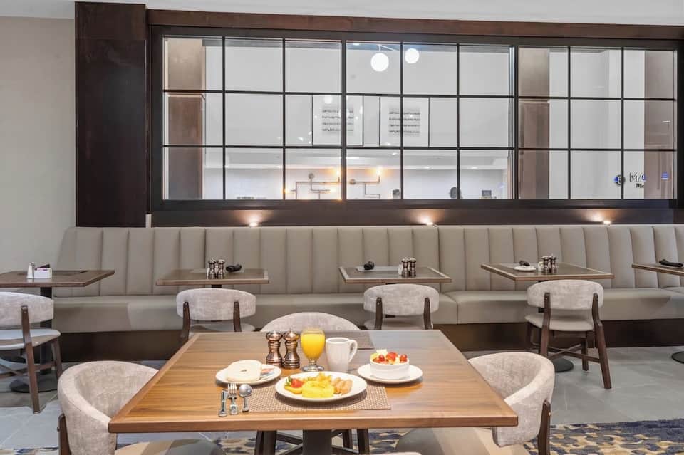 Contemporary breakfast dining room with wood tables, upholstered chairs, beige booth seating, and large windows