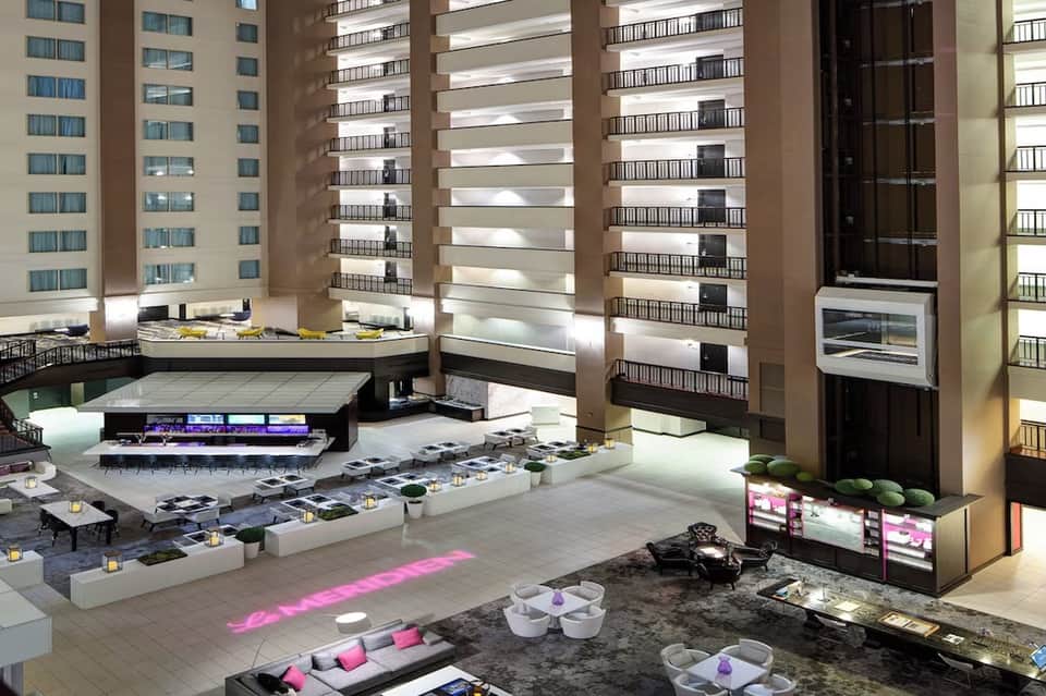 Multi-story hotel atrium with modern architecture, neon lighting, and ground-level lounge seating