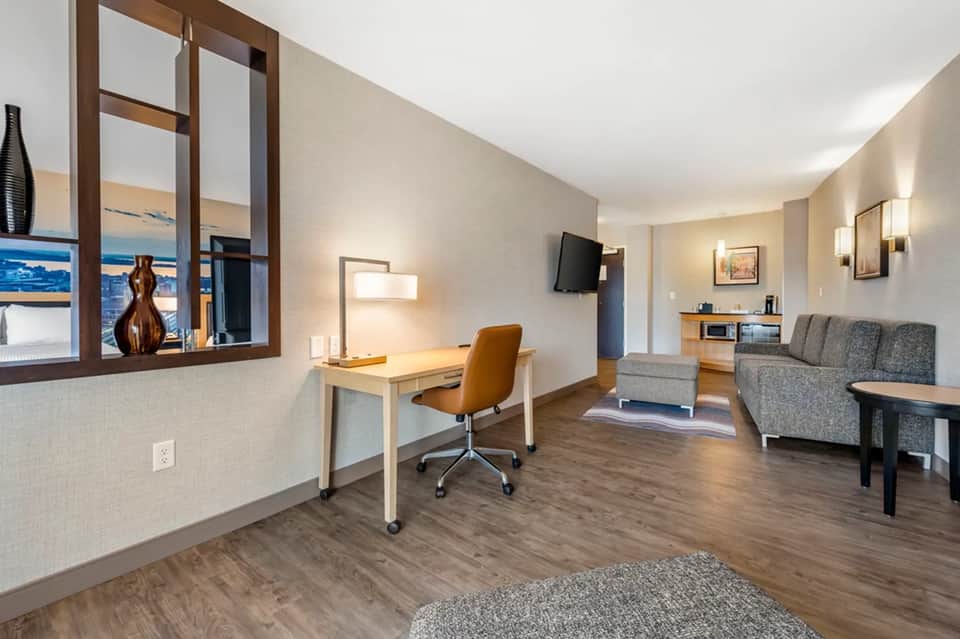 Modern hotel suite with ocean view window, work desk, comfortable seating area, and contemporary décor