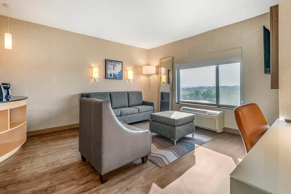 Hotel suite with gray sofa, armchair, window seating, and landscape view of countryside