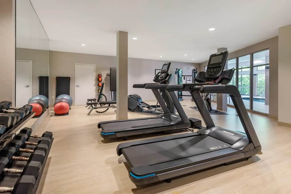 Fitness center with treadmills, exercise equipment, mirrors, and large windows overlooking grounds