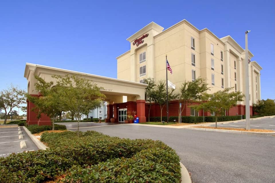 Hampton Inn hotel exterior with cream-colored building and red brick base under blue sky