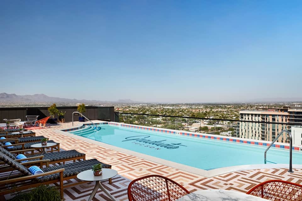 Rooftop pool with geometric patterned deck, lounge chairs, and distant desert mountain landscape view