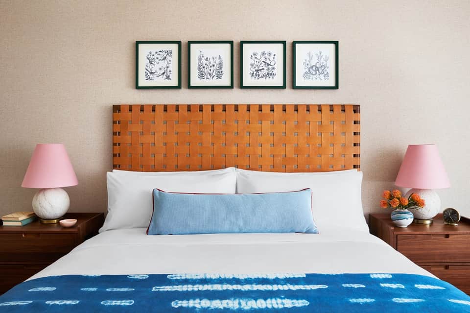 Bedroom with orange woven headboard, white bedding, blue throw pillow, and pink nightstand lamps