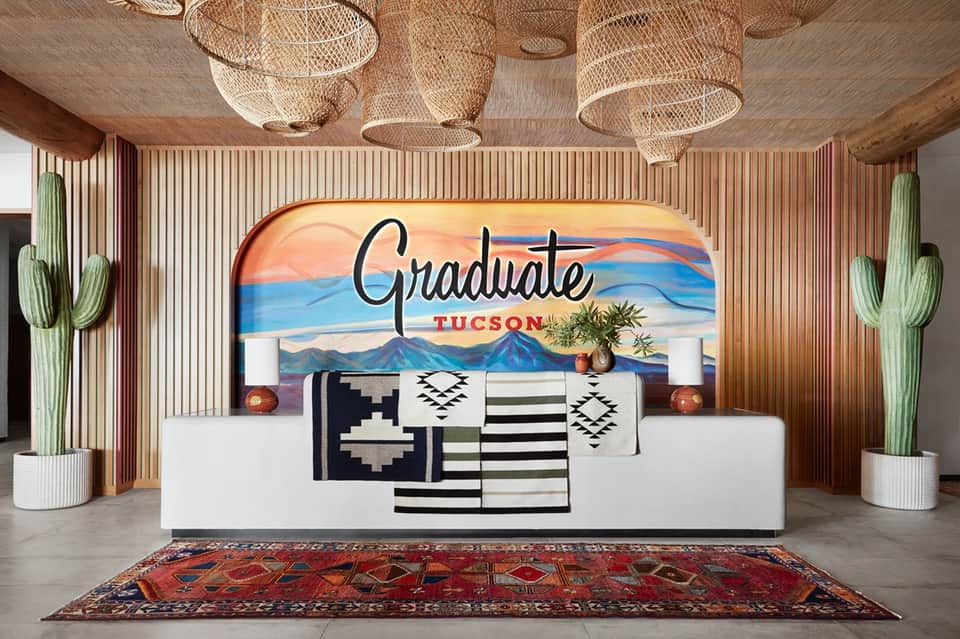 Modern hotel lobby with Graduate Tucson sign, woven pendant lights, cacti, and colorful area rug