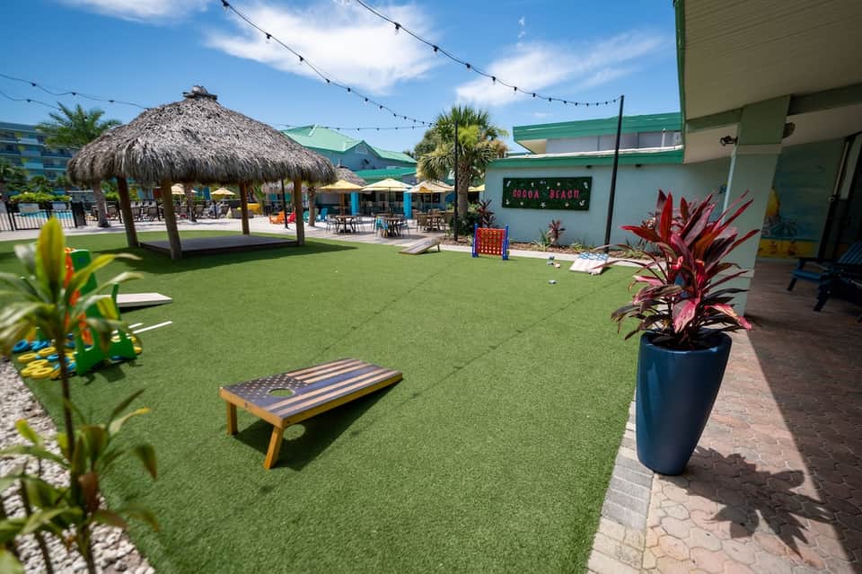 Outdoor recreation area with artificial turf, cornhole game, tiki bar, and string lights