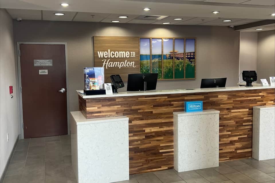 Hotel reception desk with wooden accent wall, welcome signage, Hilton branding, and check-in counter