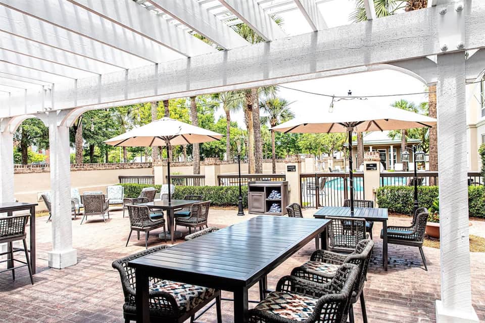 Shaded patio area with dining tables, umbrellas, white pergola, and resort grounds
