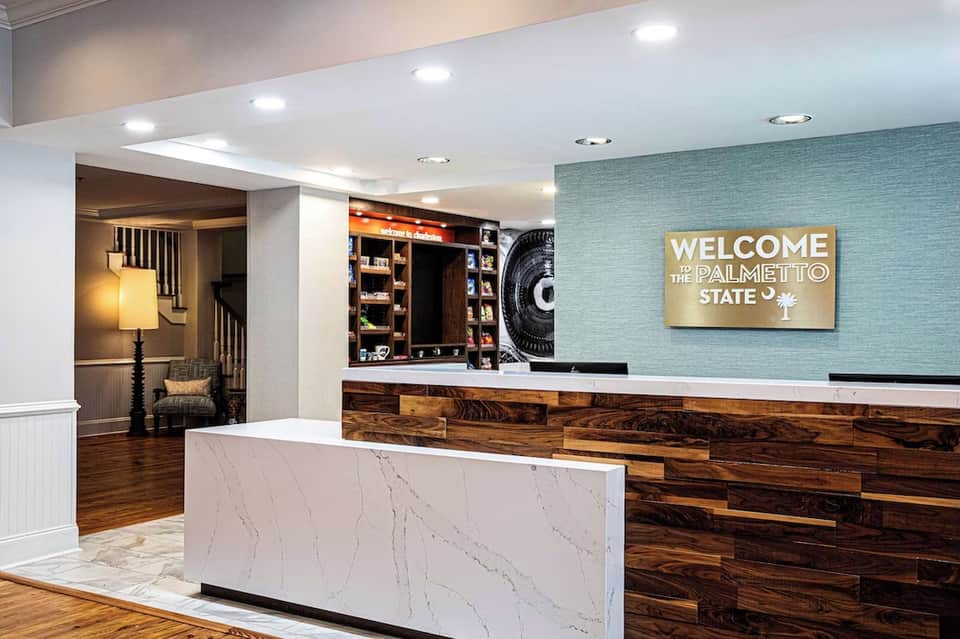 Hotel check-in desk with marble counter, teal accent wall, and welcome signage