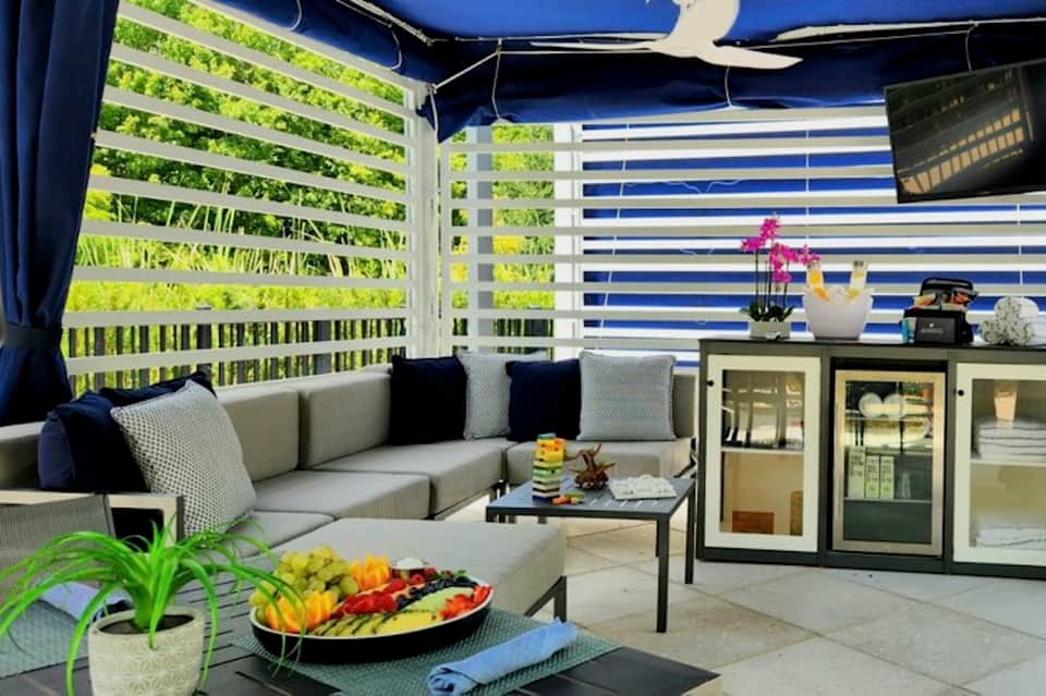 Outdoor lounge with striped blue and white motorized shades, cream seating, and potted plants