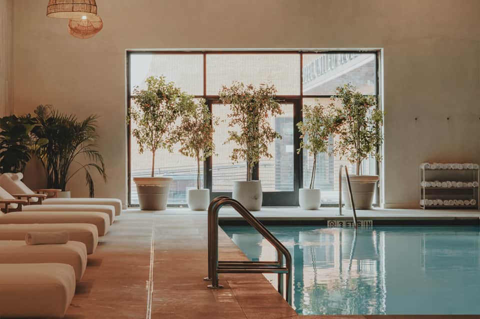 Spa pool with lounging area, large windows overlooking city, potted plants, and rope pendant light