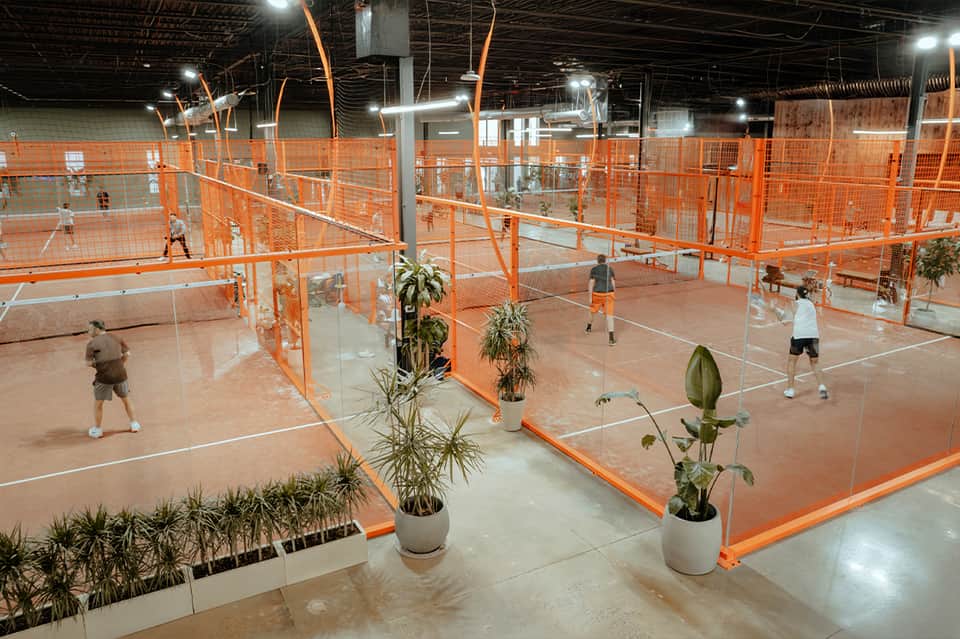Indoor pickleball facility with multiple orange courts and potted plants