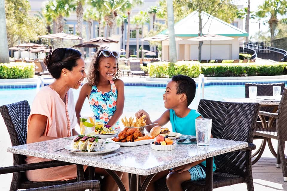 Family dining poolside with food and drinks on granite table overlooking resort pool