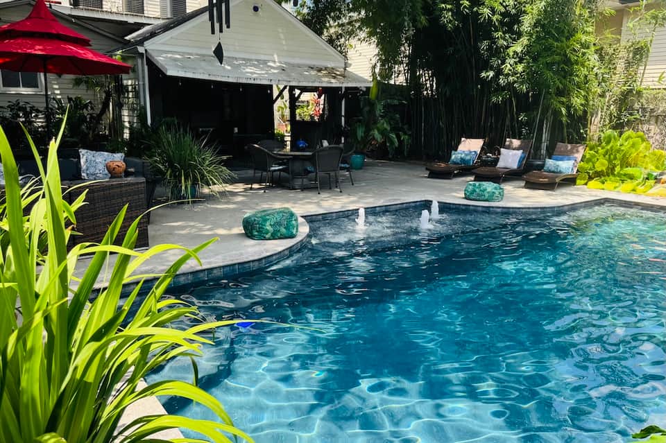 Resort backyard with curved swimming pool, tropical plants, red umbrella, and covered lounge seating area