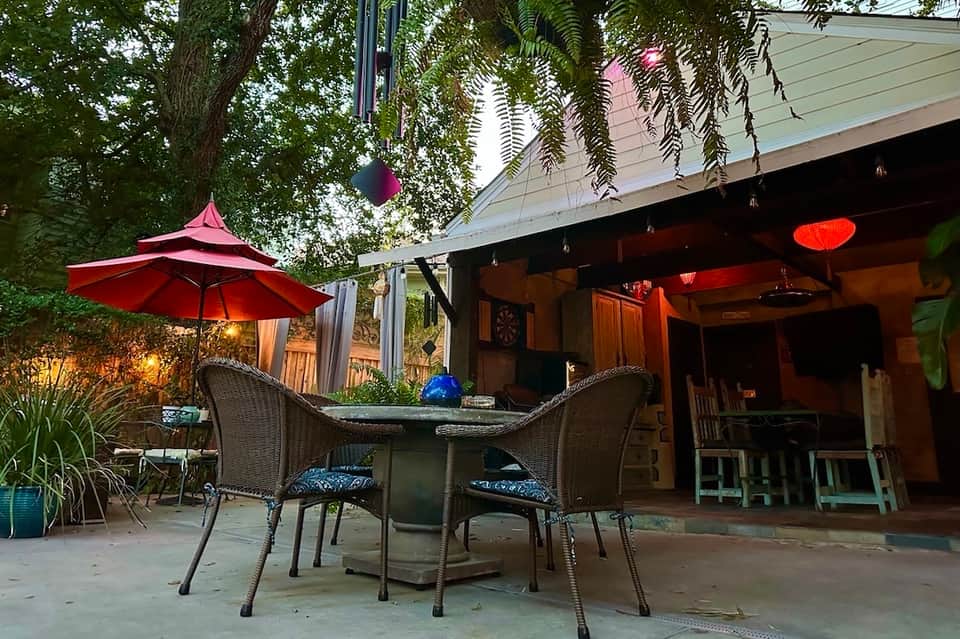 Outdoor patio area under pergola with red umbrella, wicker lounge chairs, and warm ambient lighting