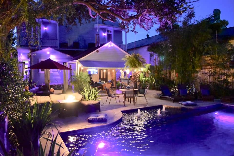 Night view of resort courtyard with glowing purple accent lighting, pool, pergola, and lounge seating areas