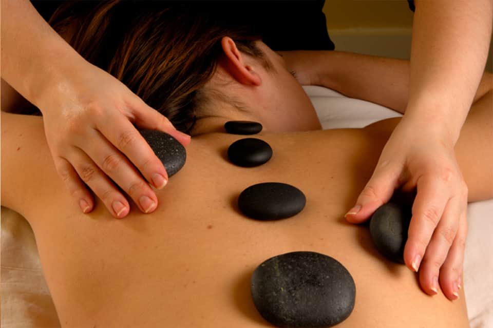 Spa therapist performing hot stone massage on client's back