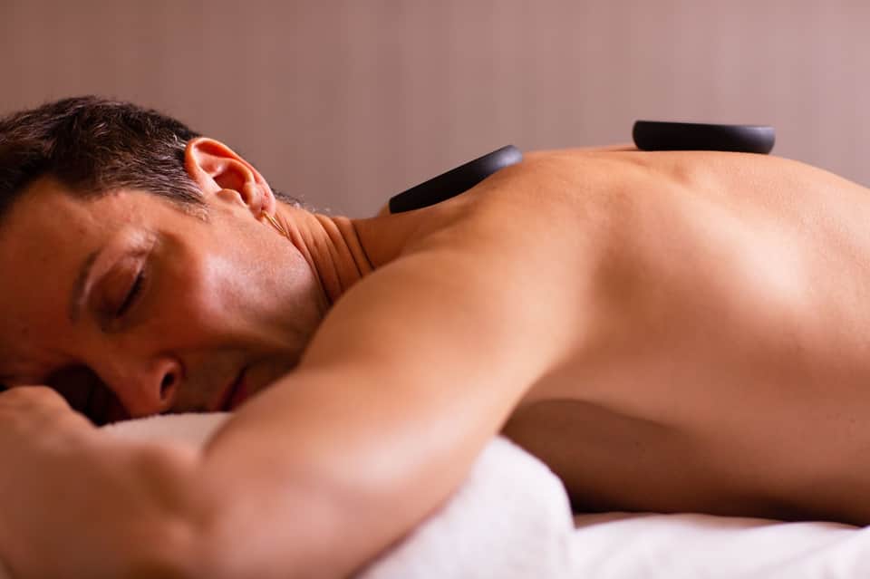 Spa treatment: man receiving hot stone massage on relaxation bed with eyes closed