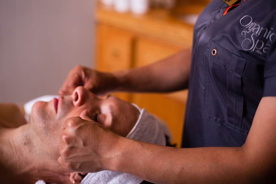 Spa therapist performing facial massage on male guest in wellness treatment room