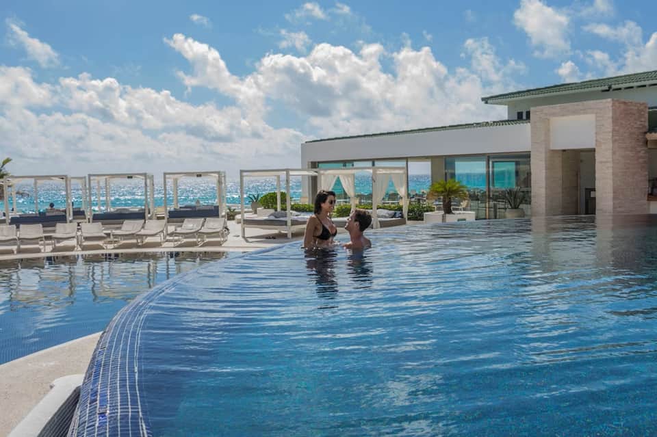 Resort infinity pool with ocean views, guests swimming, loungers, and modern coastal architecture
