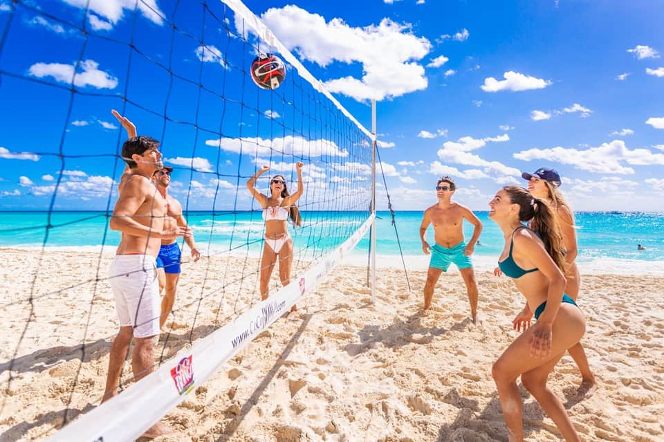 Young adults playing beach volleyball on sandy shore with turquoise ocean