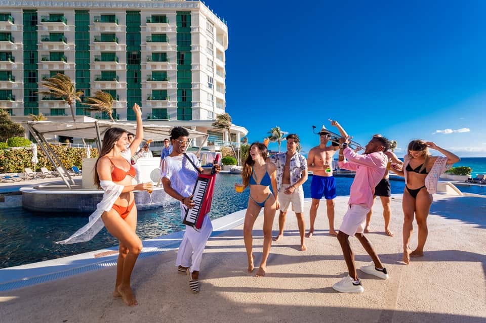 Pool party with guests dancing and celebrating by the water with hotel building and ocean backdrop
