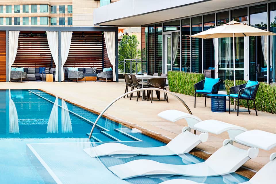 Luxury resort pool deck with white lounge chairs, cabanas with curtains, and modern building architecture
