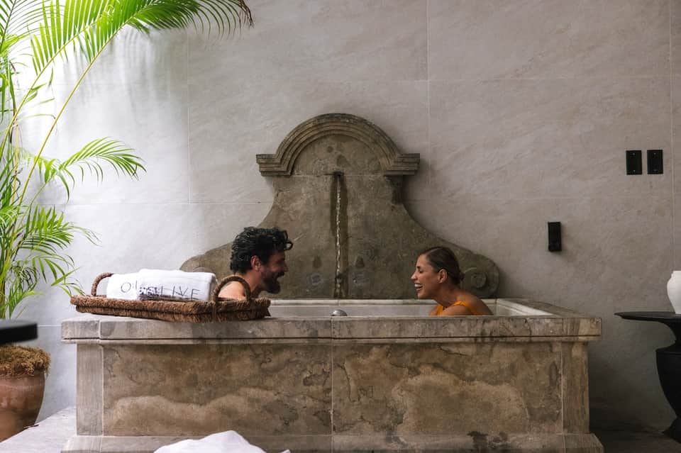 Couple enjoying a stone spa tub with decorative arch feature and plants