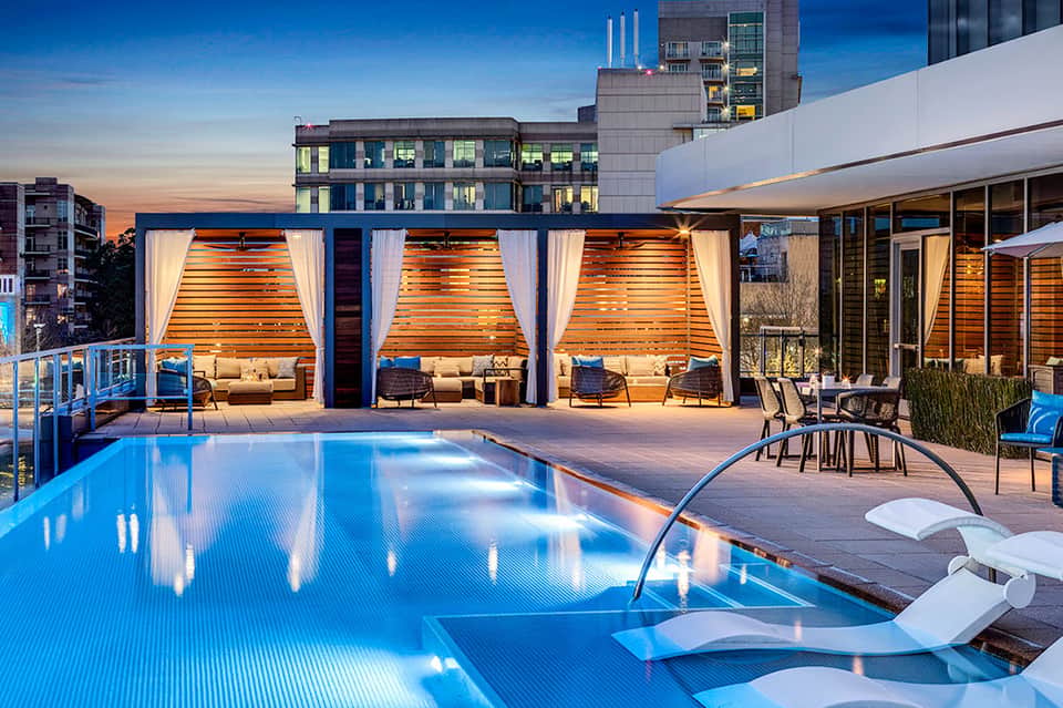 Illuminated poolside cabanas and lounging area at dusk with city skyline views