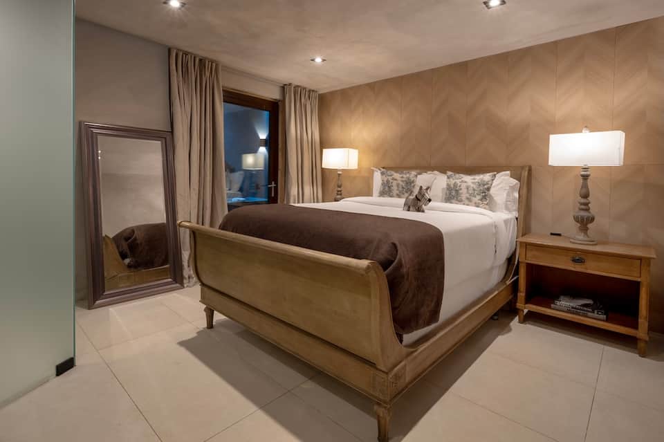 Upscale hotel bedroom with wooden bed frame, neutral tones, and modern lighting fixtures