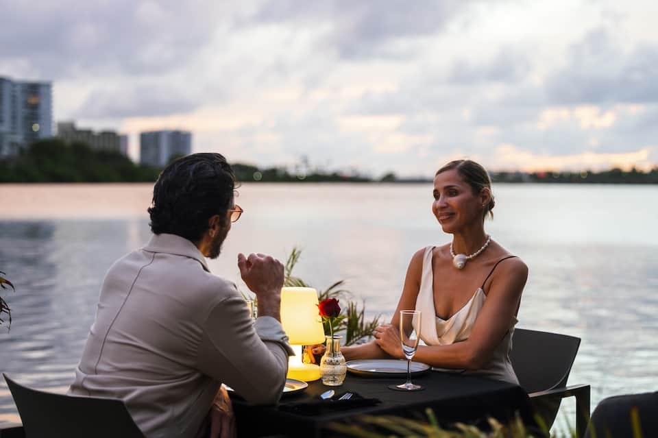 Couple dining at waterfront table with candles and water views at dusk