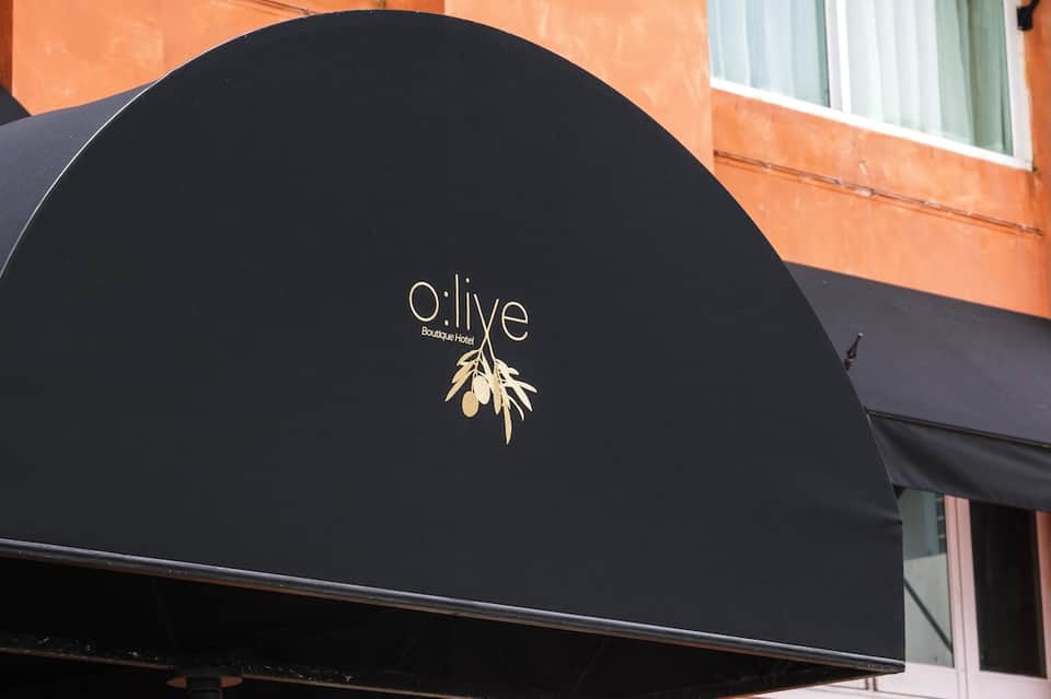 Black awning with 'o:live' boutique hotel branding and gold olive leaf logo on building facade