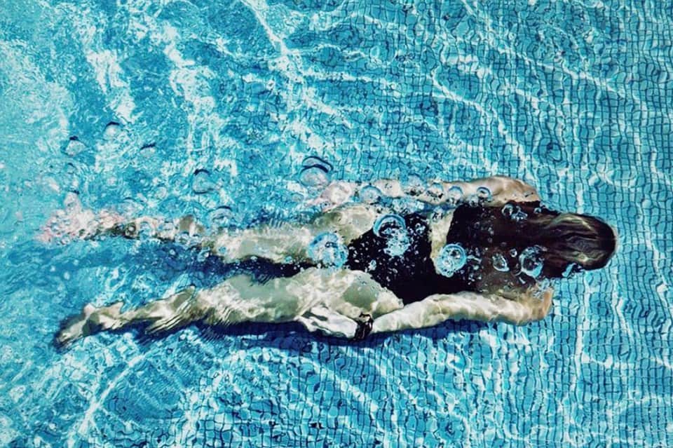 Overhead view of swimmer doing freestyle stroke in clear turquoise pool with tile pattern visible