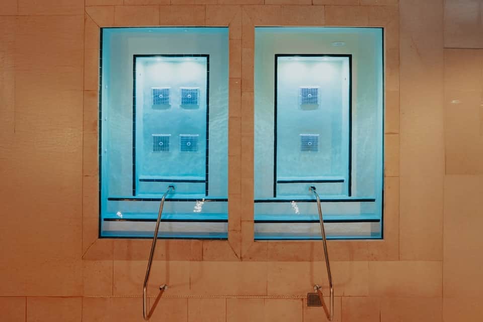 Two rectangular windows showing indoor swimming pool with underwater jets and lounge chairs