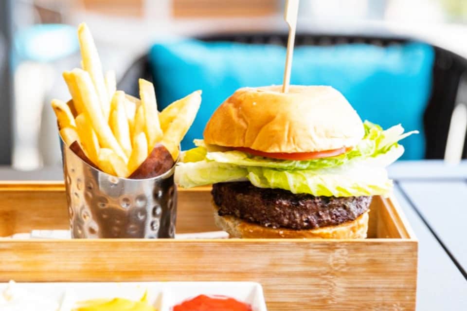 Gourmet burger with lettuce and tomato served with french fries on wooden tray