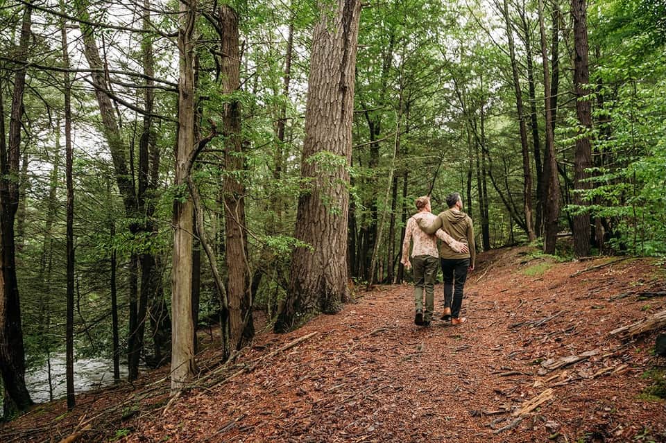 Couple jogging on wooded forest trail near water with tall trees overhead
