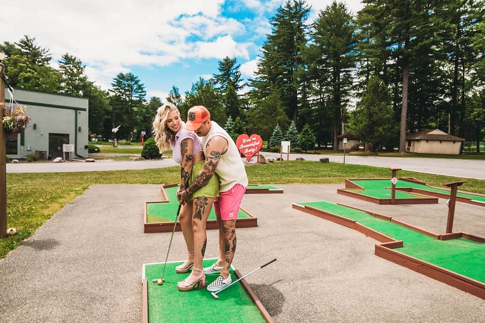 Couple playing mini golf on green course with forest background and modern resort building