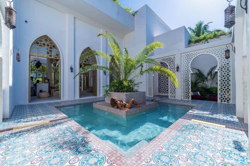 White courtyard with turquoise pool, arched doorways, decorative tile, and palm plants
