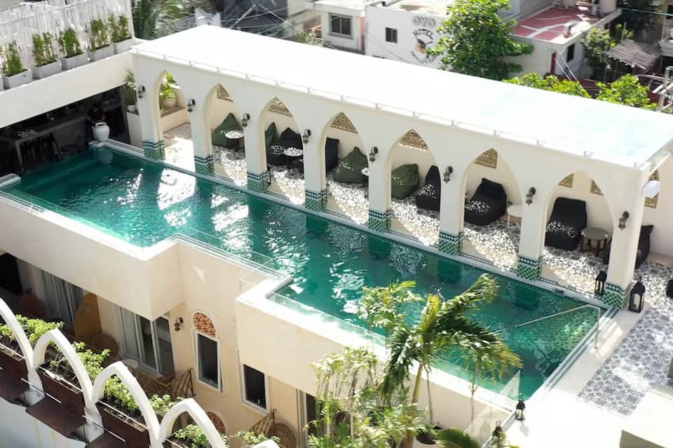 Rooftop pool with turquoise water, white arches, lounging cabanas, and city views