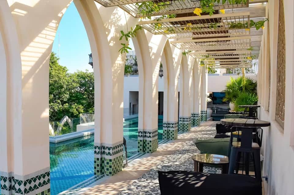 Covered poolside corridor with white columns, green tile accents, and shaded lounge area