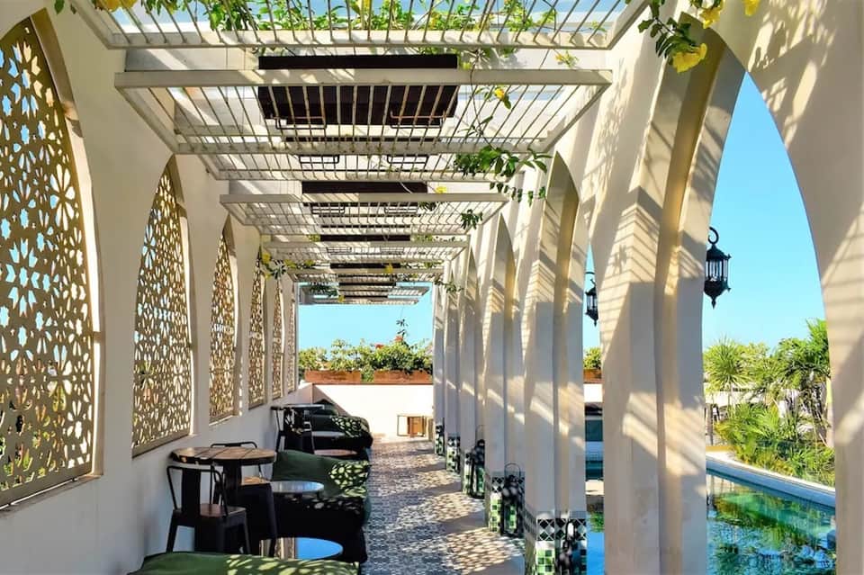 Covered pergola walkway with geometric lattice panels, seating area, and pool view beyond