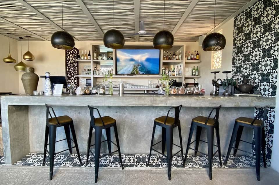 Modern bar with concrete counter, black bar stools, geometric pendant lights, and patterned wall