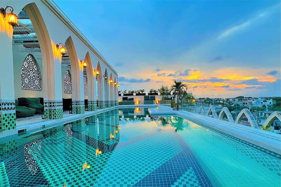 Rooftop pool at dusk with Moroccan arches, golden lanterns, and sunset sky reflection