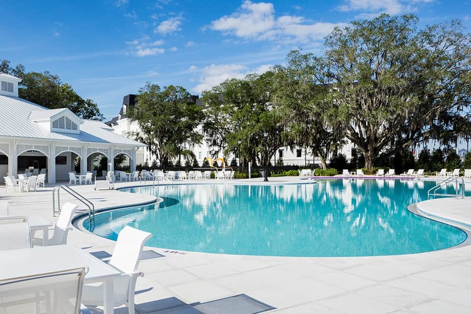 Large curved resort pool with white cabana, lounge chairs, oak trees, and manicured lawn