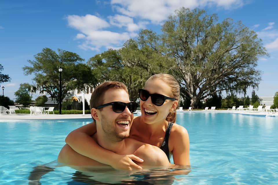Young couple smiling in resort pool with lounge chairs and trees visible in background
