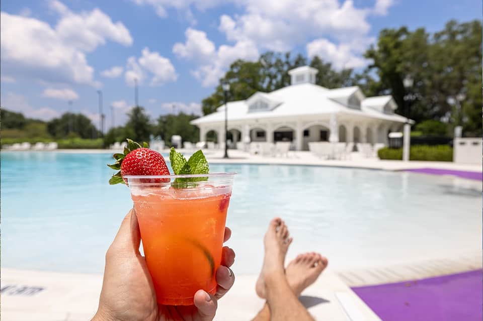Refreshing strawberry mojito cocktail held poolside with white pavilion and purple loungers in background