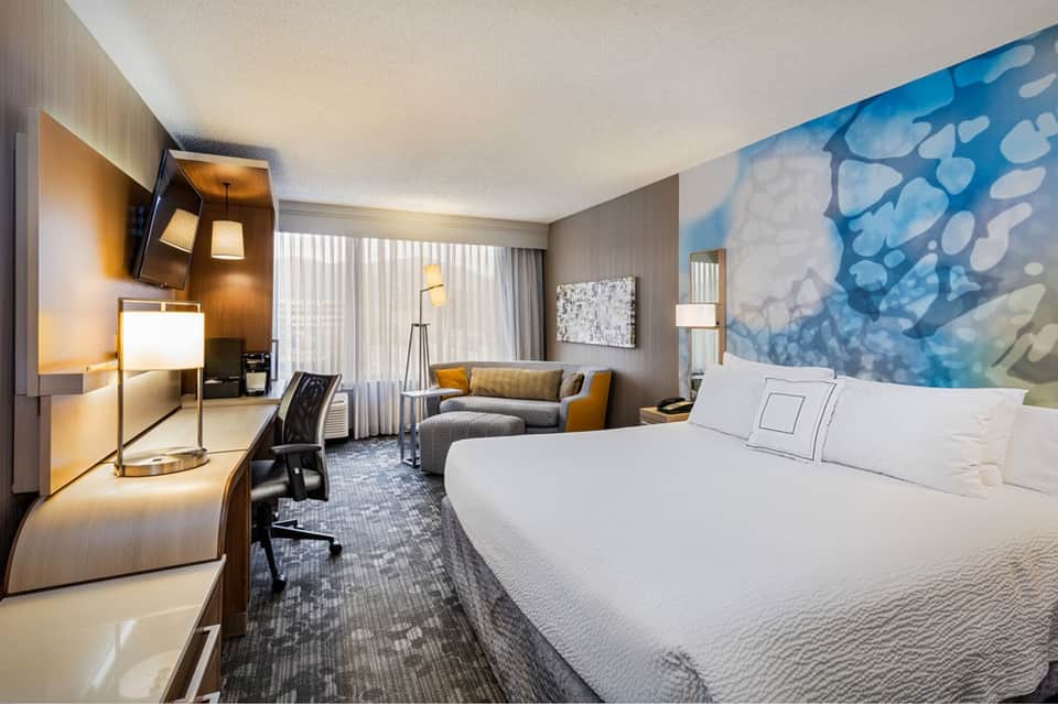 Contemporary hotel bedroom with king bed, work desk, armchair, artistic wall mural, and warm ambient lighting
